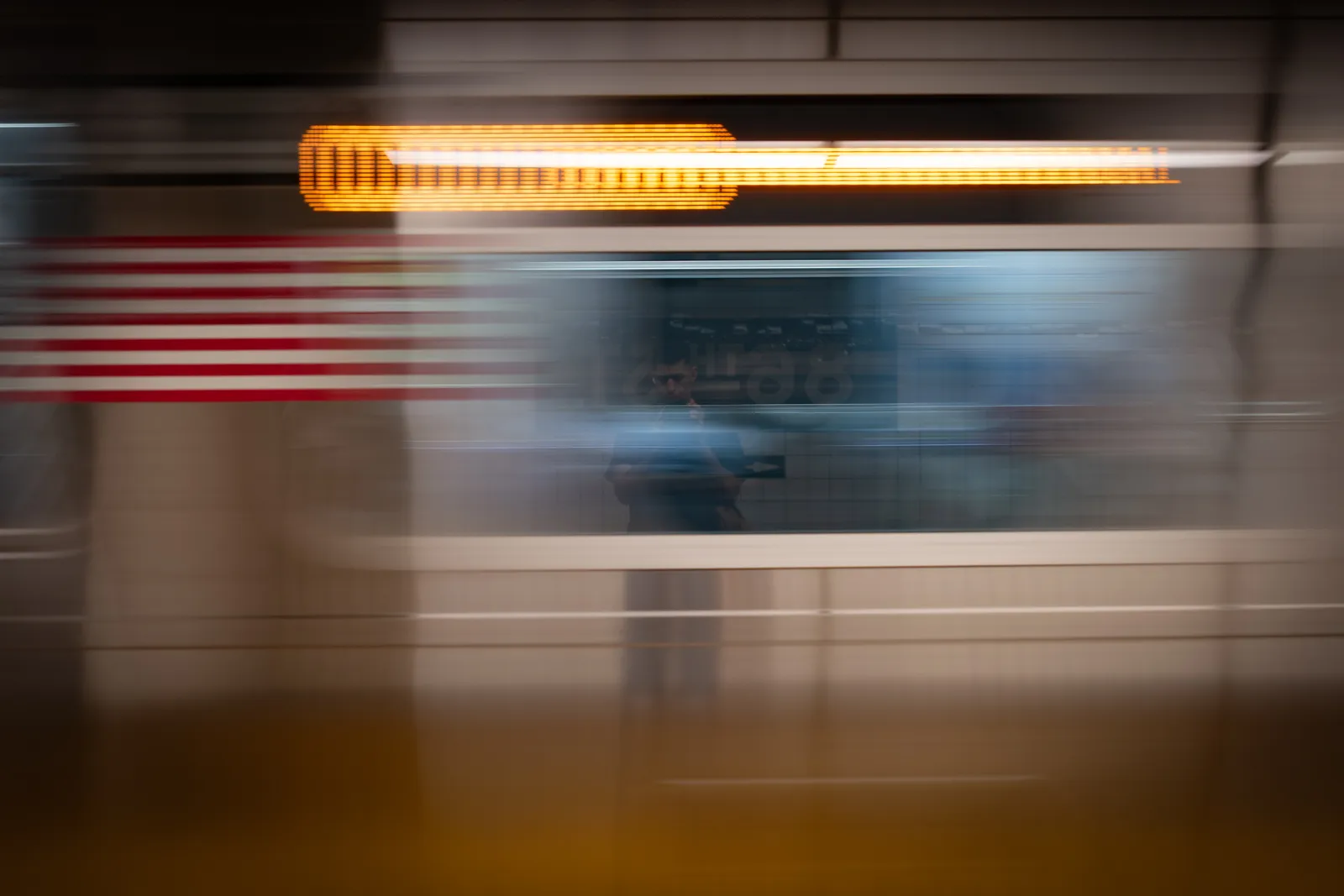 A heavily motion-blurred photograph featuring horizontal streaks of colored light in an abstract urban setting.